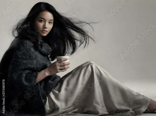 Moody portrait of an elegant woman with flowing hair holding a cup against a minimalist background