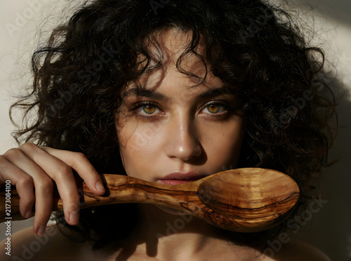 Artistic portrait of a beautiful woman with curly hair holding a rustic wooden spoon