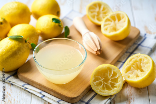 Fotografie Bowl with fresh lemon juice, squeezer and ripe lemons on white table, close up
