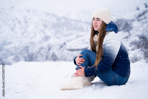 Foto Woman sitting on snowy ground outdoors after twisting her ankle while walking in winter, holding her leg because of an injury