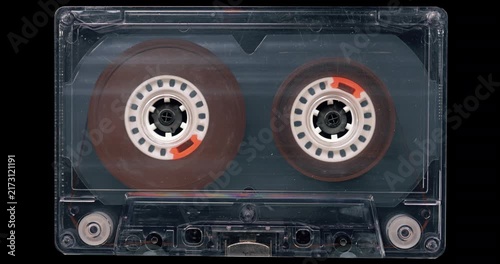 Old Transparent Audio Cassette with Reels Turning.
Exposed magnetic tape reels rotate smoothly inside a clear unlabeled cassette.