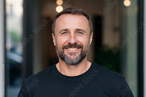 Middle aged man with short hair and a beard smiling directly at the camera outdoors
