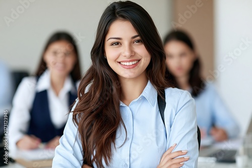 Smiling young woman in a blue shirt with arms crossed sitting in a bright modern office space