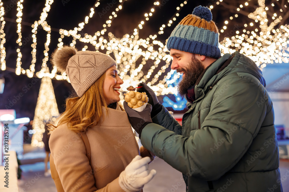 Obraz premium Couple feeding each other with sweet snacks while enjoying winter holiday season outdoors in the city