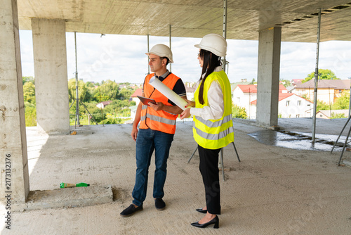 Project manager and builder discuss large floor plan. Builder explains layout features and points out functional areas holding tablet