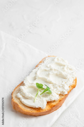Foto Toasted bread slice topped with creamy ricotta cheese and fresh microgreens on a white plate, showcasing a simple yet elegant food presentation