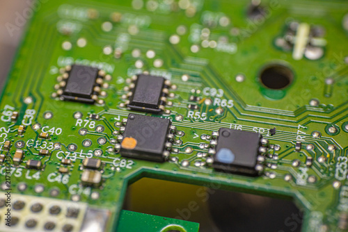 Close-up view of a green printed circuit board featuring multiple integrated circuits, resistors, and soldered connections, showcasing intricate electronic components and pathways
