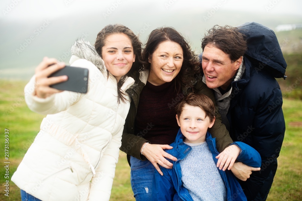 Fototapeta premium Family taking a selfie outdoors on a foggy day, all smiling warmly.