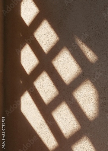 Close-up of a wall with a diagonal pattern of light rays shining through it. the light rays are arranged in a grid-like pattern, creating a shadow on the wall.