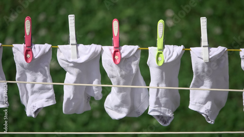 White socks hanging on clothesline with colorful clothespins drying in sunny garden