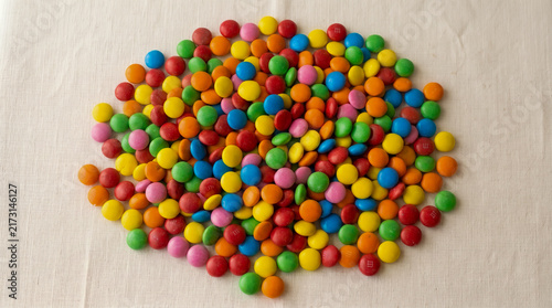 Top-down view of a vibrant pile of multi-colored sugar-coated chocolate candies neatly gathered on a neutral beige woven linen surface.