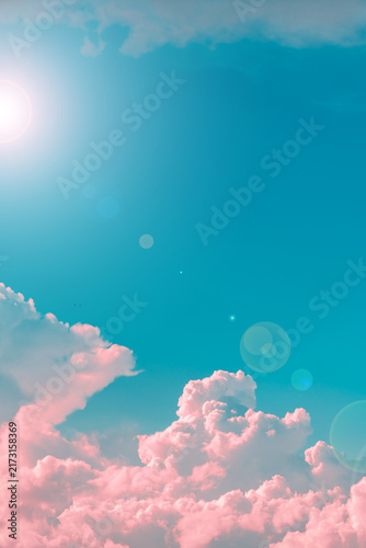 Fluffy pink cumulus clouds filling a vibrant blue sky, creating a serene and ethereal atmosphere with a bright sun flare appearing from the upper left