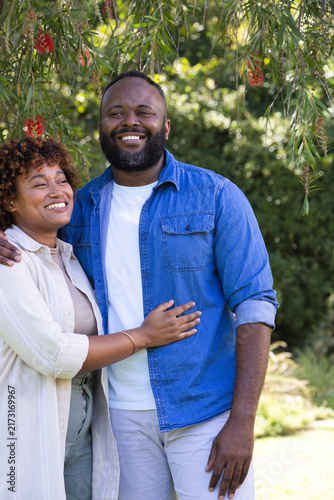 African American couple standing under tree in park with red blooms, wearing denim and beige