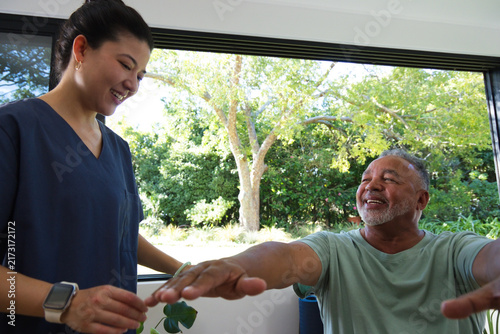 Canvas Print Asian caregiver in scrubs guiding African American senior doing arm stretch with
