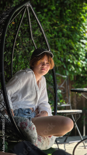Teen Sitting in Hanging Swing Chair in Garden Patio
