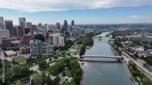 panning 180° left from Peace Bridge along Skyline of Downtown Calgary ( Alberta, Canada)  to Centre St Bridge, with Prince’s Island Park and Bow River below and skyscrapers in front - 4k aerial video