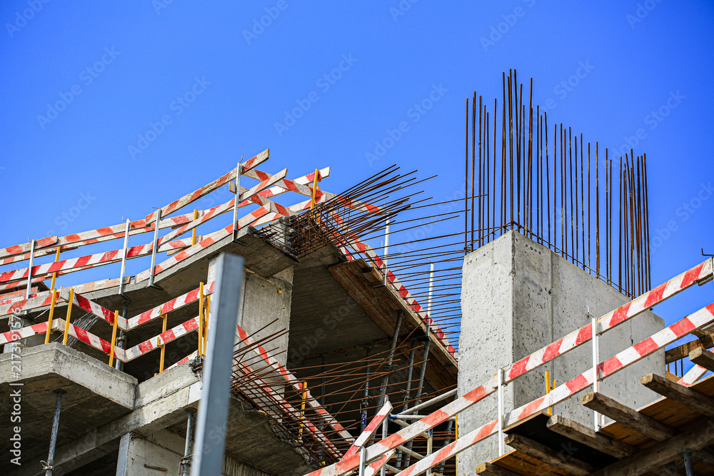 Fototapeta premium Unfinished concrete building structure with exposed rebar columns and striped safety tape under sunny sky, construction site renovation progress