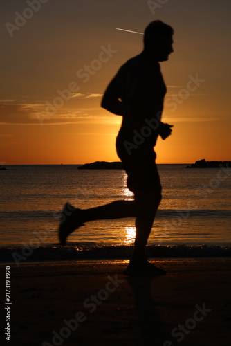Konstfotografi Silhouetted runner in mid stride on the beach against a glowing orange sunrise s