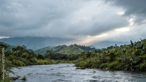 Flowing river water through tropical green valley under dramatic cloudy sky