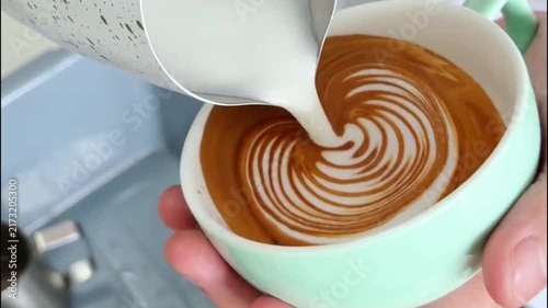 Barista Pouring Steamed Milk into Light Green Cup to Create Winged Heart Latte Art