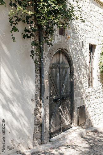 Cobblestone street and antique door in a Mediterranean village. Old weathered wooden door set in an arched stone doorway of a traditional house in Alaçatı, a historic town on the Aegean coast, Turkey.