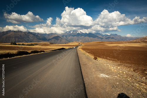View of the long asphalt road leading towards the snow-capped Huascaran mountain range under a dramatic cloudy sky in Yungay Province, Ancash, Peru.