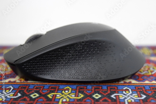 Принти на полотні Side profile view of a black ergonomic wireless optical mouse with textured rubber side grip resting on a colorful traditional carpet mousepad
