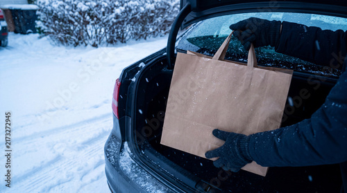 Person placing paper shopping bag into car trunk in winter