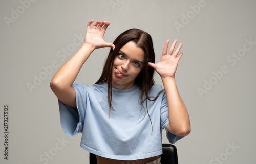 Konstfotografi Young woman making a silly face, sticking out tongue and raising hands playfully