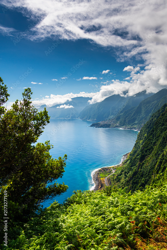 Obraz premium Stunning panoramic view of the lush green coastal cliffs and turquoise Atlantic Ocean from a viewpoint in Madeira near Ribeira da Janela under a bright summer sky.