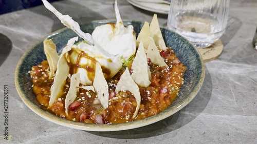 Cutting open a cheese ball dumpling in chili sauce Savory spicy tomato dip topped with creamy ice cream, crisp tortilla chips, pomegranate seeds, and sweet sauce in a ceramic bowl.