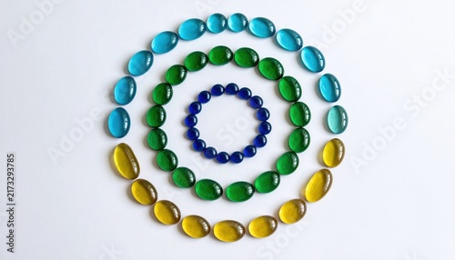 Vibrant circular arrangement of colorful oval glass beads and pebbles on a white background