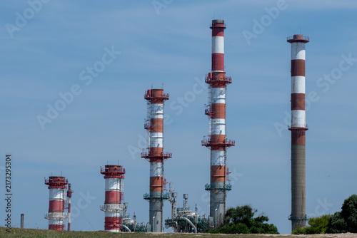 Industrial oil refinery smokestacks with red and white stripes behind green hill in Portugal