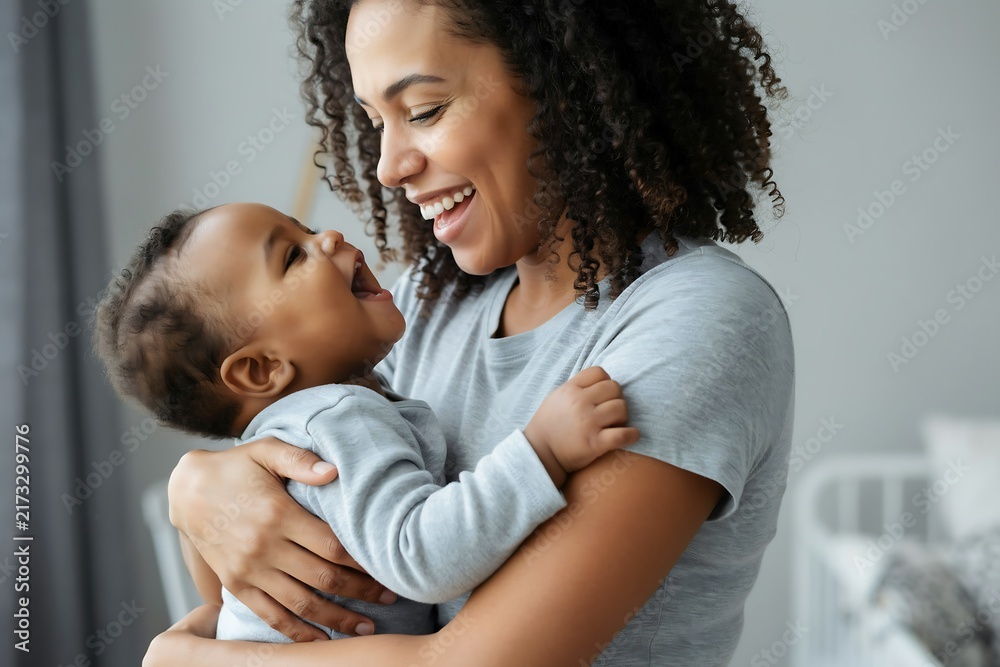 Obraz premium Happy mother holding her laughing baby boy in a cozy home nursery setting