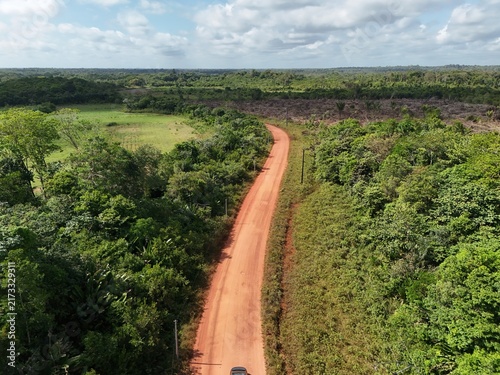 Fotografie Aerial drone view of a red dirt road crossing lush tropical vegetation and forest in French Guiana, South America