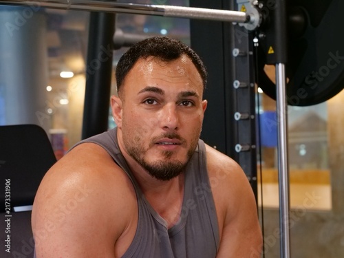 Canvastavla Sweaty and exhausted muscular man taking a break after an intense workout set in a gym, looking directly at the camera with serious gaze