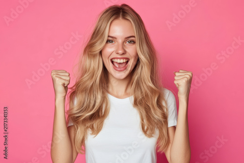 Happy young woman celebrating with her fists raised in front of a pink background