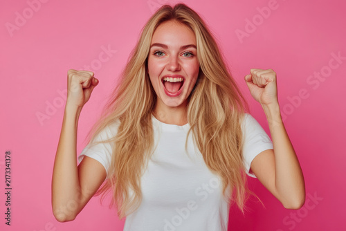 Joyful young woman celebrating with raised fists against a pink background