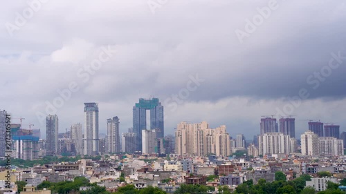Panning shot of gurgaon cityscape with modern skyscrapers, high-rise construction, dense buildings, and dramatic heavy clouds during the monsoon season.