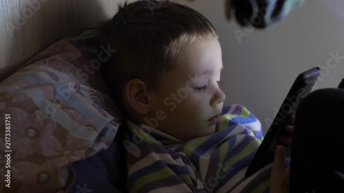 A little boy sits in a closet and plays with a telephone