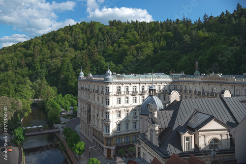 Fotografie Tepla river flowing through Karlovy Vary with Hotel and forest in background in