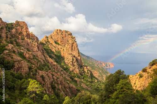 Rainbow over the red granite cliffs of Calanques de Piana, with Mediterranean Sea and dramatic coastal scenery on Corsica, France.