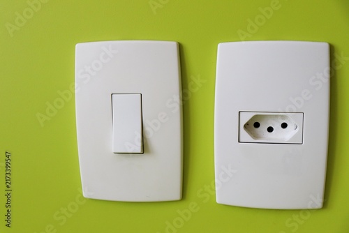 White light switch and electrical socket on a green wall. Home energy, electrical outlet, and interior power fixture.