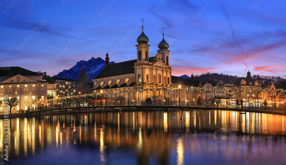 Fototapeta premium Splended sunset over the Jesuit church with Pilatus mountain at background in the evening and Rathaussteg in Christmas illumination, Switzerland