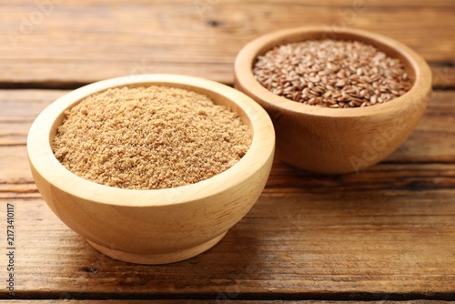 Flax seeds and powder in bowls on wooden table, closeup