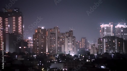 Panning night shot of lit up gurgaon cityscape with modern skyscrapers, high-rise construction, dense buildings, showing the rapid growth and urbanization of this city