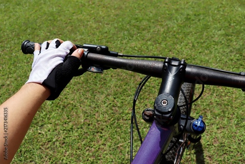 Close-up of a cyclist hand wearing a riding glove holding a bicycle handlebar with brake lever and gear shifter outdoors. Cycling concept.