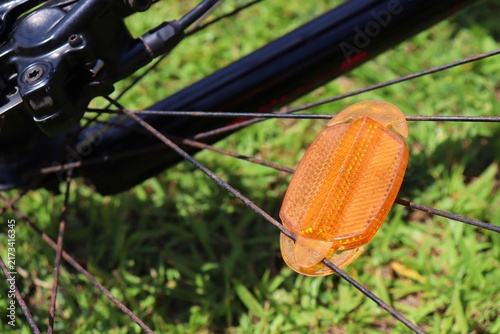 Orange bicycle spoke reflector mounted on a bike wheel. Cycling safety equipment, night visibility, and road precautions.
