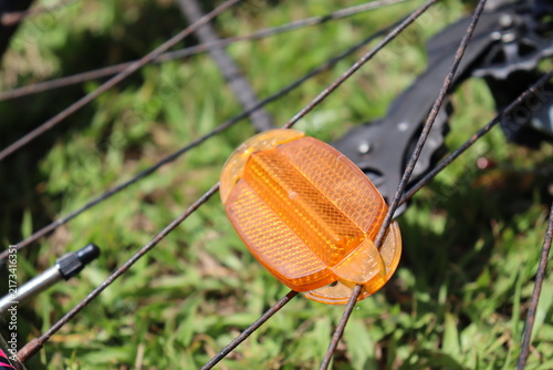 Orange bicycle spoke reflector mounted on a bike wheel. Cycling safety equipment, night visibility, and road precautions.