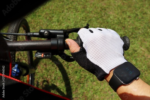 Close-up of a cyclist hand wearing a riding glove holding a bicycle handlebar with brake lever and gear shifter outdoors. Cycling concept.